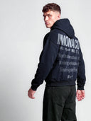 Monaco Aesthetic navy streetwear hoodie on model, angled back view with light gray branding and large text graphic.
