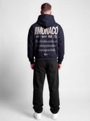 Navy tapered hoodie worn by model, back view with cream Monaco typography and large urban lifestyle statement.