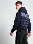 Navy Monaco athleisure hoodie worn by model, angled back view with lavender logo stack and statement typography.