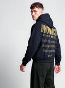 Navy Monaco athleisure tapered hoodie on model, angled back view with gold branding and statement graphic.