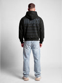 Black tapered hoodie worn by model, back view showing tonal dark Monaco branding and ribbed waistband.