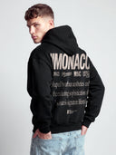 Monaco Aesthetic black graphic hoodie on model with cream back typography, logo stack and lifestyle statement.