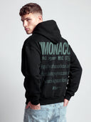 Monaco Aesthetic black hoodie on model, back view with green stacked branding and urban lifestyle statement.