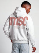 Model wears heather gray Monaco MSC hoodie, angled back view with muted coral logo and culture-inspired text.