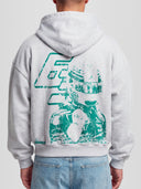 Model wearing the Racer No. 63 Heavyweight Full-Zip Hoodie in Ash Grey with teal racing driver graphic — Monaco Social Club