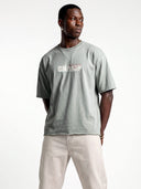 Model wearing the light grey Monaco Champ oversized tee, front view with cream lettering and colorful accents.