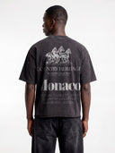 Model in dark grey Open Land tee, back view highlighting three horses and oversized Monaco typography.
