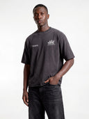 Dark grey Open Land heavyweight tee worn by model, close front view highlighting the dual chest graphics.