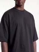 Black boxy tee on model, cropped front view showing ribbed crew neck and drop shoulders.