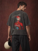 Monaco Social Club Racing Club: model seen from behind in a washed black oversized boxy raw hem tee with a motion-blur F1 driver back graphic, holding a vintage racing helmet