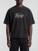 Front view of a model wearing the faded black Monaco Social Club Toronto hockey tee with white chest artwork, an oversized boxy fit and dropped shoulders.